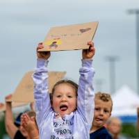 Young girl from the GVSU Children's Enrichment Center holding her "You can do it" handmade sign high in the air above her head, with her tongue sticking out